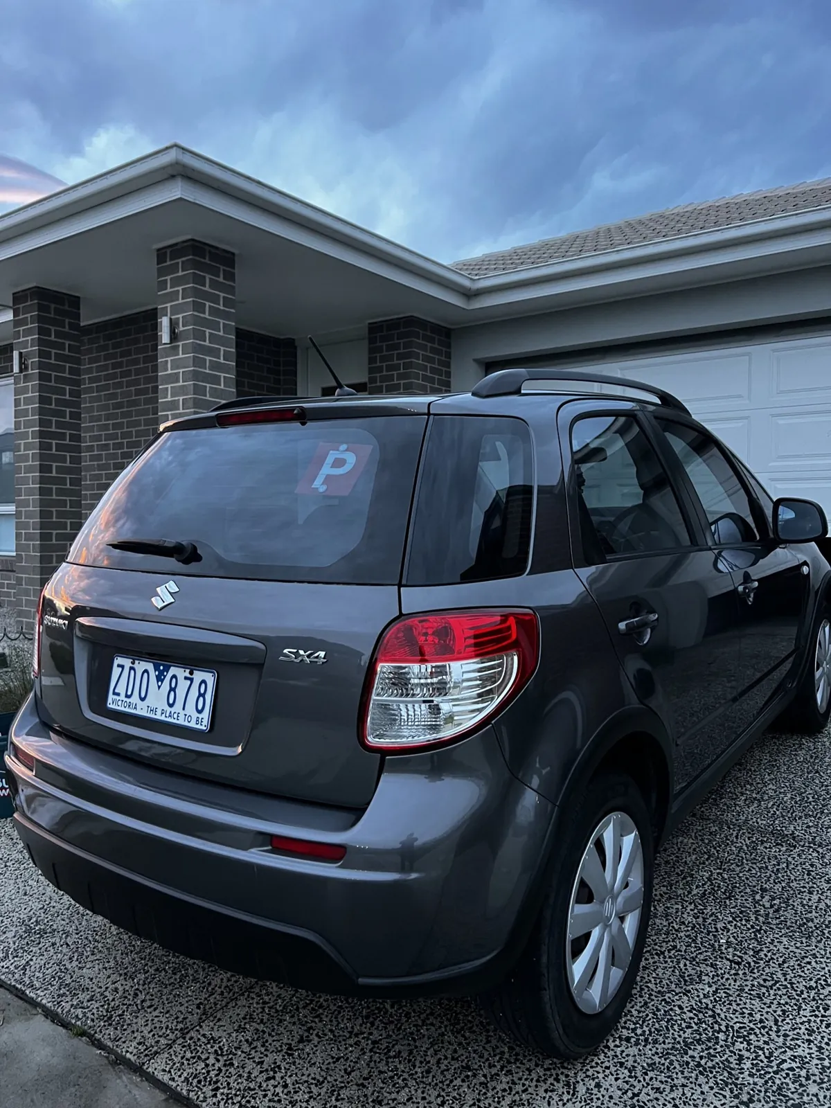 Dark Suzuki SX4 hatch detailed on a residential driveway