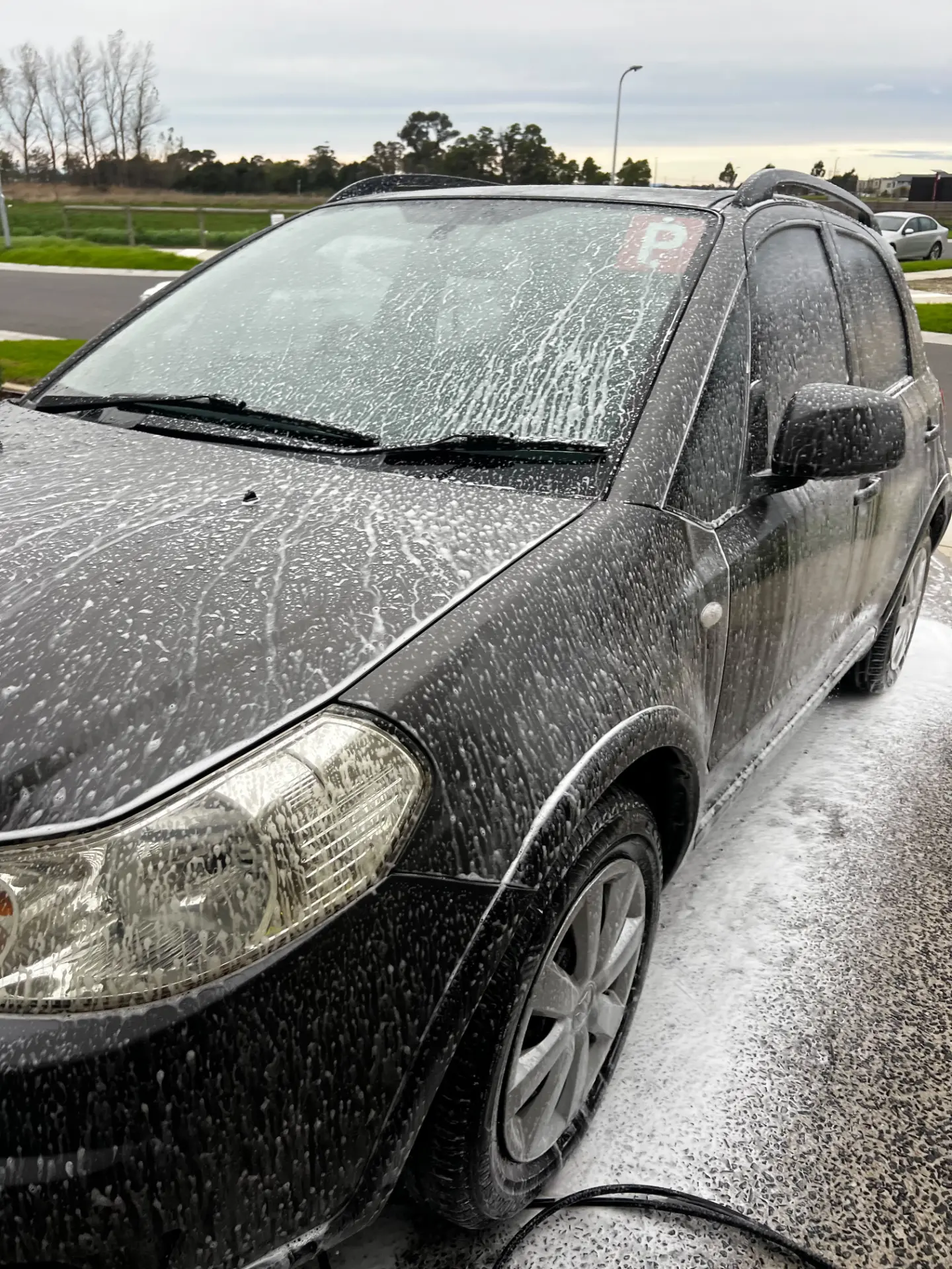 Dark vehicle covered in thick snow foam during a swirl-free maintenance wash